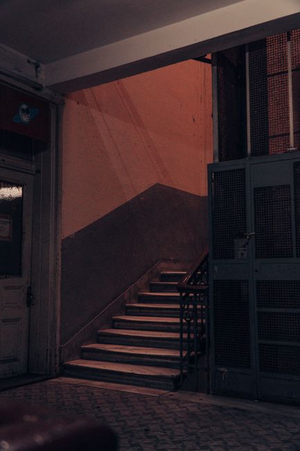 Close-up view of an external metal staircase leading to a back door on the brick facade of a building, with galvanized steel steps and handrails that show signs of corrosion and rust. The door is pain